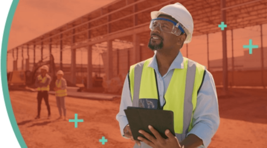Superviseur portant un gilet de sécurité à haute visibilité et un casque de protection, tenant une tablette sur un chantier de construction.
